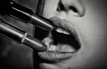 Cosmetics, lipstick. Open mouth with two lipstick touching upper and lower lips. Black and white...