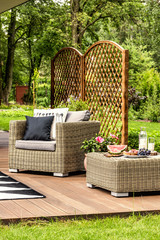 Rattan armchair with pillows and table on a terrace in a beautiful green yard