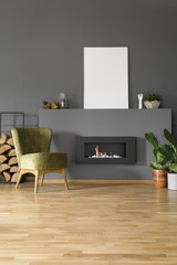 Real photo of a green armchair standing next to a bio fireplace and plants in living room interior with mockup poster