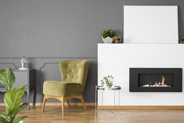 Real photo of a green armchair standing next to a bio fireplace in simple living room interior