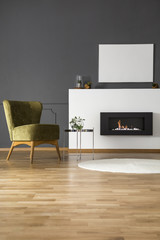 Real photo of a green armchair standing next to a bio fireplace with mockup poster in spacious living room interior