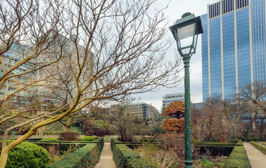 Old street lantern and green park area around orangery and urban city building towers