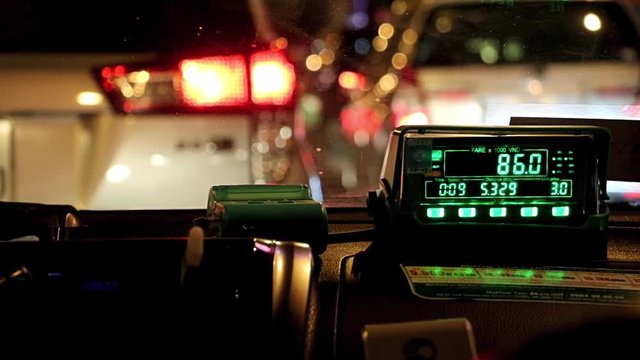 Waiting in night city traffic inside taxi car. The digital taxi meter on the dashboard of cab shows kilometer and cost.