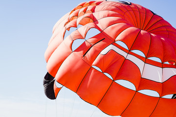 Opened orange parachute flying in a cloudless blue sky on a clear day.