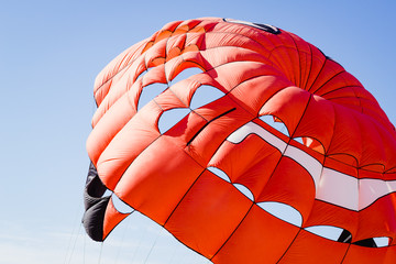 Opened orange parachute flying in a cloudless blue sky on a clear day.