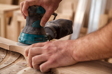 Close up of an young man builder carpenter equals polishes wooden board with a  random orbit sander...