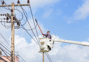 Electrician repairing wire of the power line with bucket hydraulic lifting platform on blue sky 