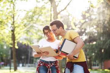 Young student couple going to college class.They walks trough university campus and reading a book.