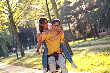 Obraz premium Young student couple making fun at the campus yard.man carrying his girlfriend on his back.
