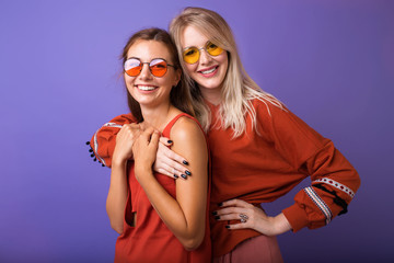 Studio lifestyle portrait of two best friends hipster girls wearing stylish bright orange outfits, dresses and sweater,sunglasses.Two beautiful young women in casual clothes in studio.