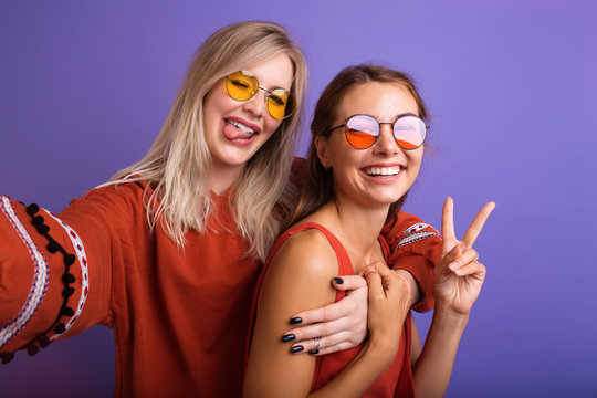 Studio lifestyle portrait of two best friends hipster girls wearing stylish bright orange outfits, dresses and sweater,sunglasses.Two beautiful young women in casual clothes in studio.