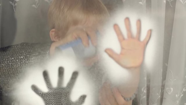 Mom and his son are being painted on the window with artificial snow, Mom is spraying artificial snow onto the child's hand and there is a trace of the palm on the window.