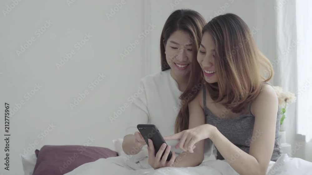 Wall mural beautiful young asian women lgbt lesbian happy couple sitting on bed hug and using phone together be