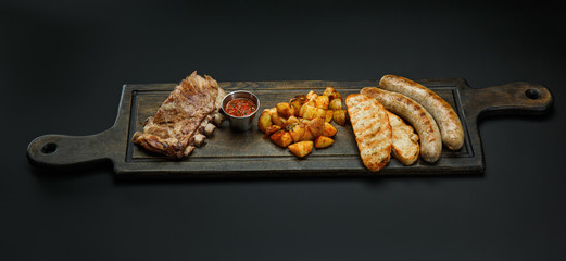 Board with sausages; Ribs, potatoes and sauce for beer isolated on a black background