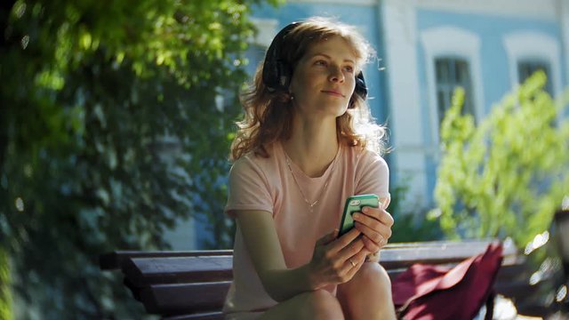 woman rollerblading and listening to music on headphones on the phone in the park