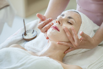 Young beautiful girl in mask for face relaxing in spa salon .woman treatment  massage with facial...