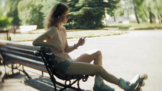 woman rollerblading and listening to music on headphones on the phone in the park