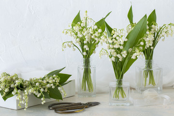 on the table lilies of the valley in glass vases, lilies of the valley in a box, scissors and ribbon