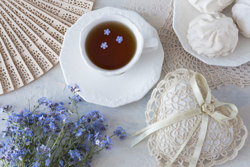 on a light table a fan, a cup of tea, forget me nots, marshmallows,