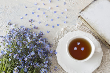 a bouquet of flowers forget-me-nots on a light table and a cup of tea and a book