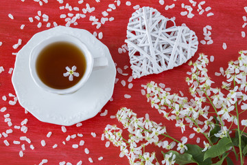 on a red background a branch of cherry, a cup of tea and a decor heart of white twigs
