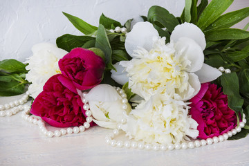 a bouquet of white and pink peonies lies on a table and beads of pearls