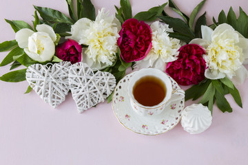 Obraz na płótnie Canvas on a pink background peonies, a cup of tea, two white hearts and marshmallows