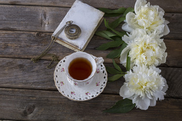 on a wooden background white peony book, cup of tea and pocket old clock