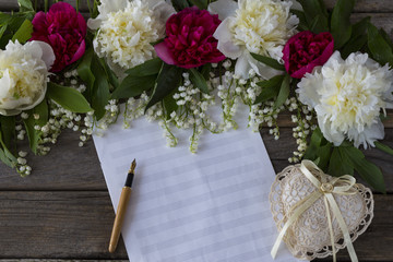 on a wooden background peonies and lilies of the valley, paper for notes, fountain pen and heart made of lace