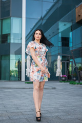 portrait of young successful girl with long brunette hair, wearing white dress with flower on the urban background