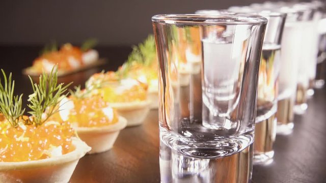 Pour the vodka in two glasses on the table with tartlets with red caviar