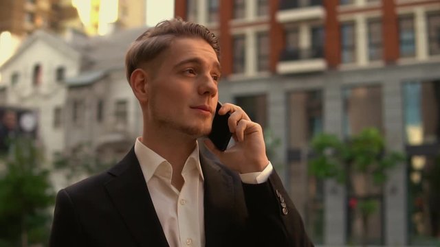 Atrractive bearded caucasian businessman using mobile phone for a small talk. Manager wears black suit and white shirt.