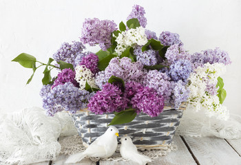 a bouquet of lilac in a basket on a wooden table and two white doves - a festive background
