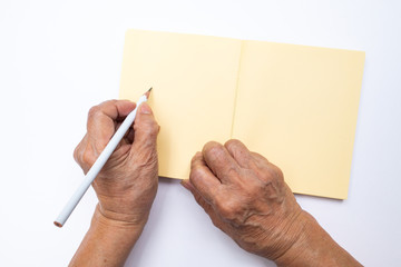 Senior woman's left hand with white pencil writing on notebook isolated on white background,...