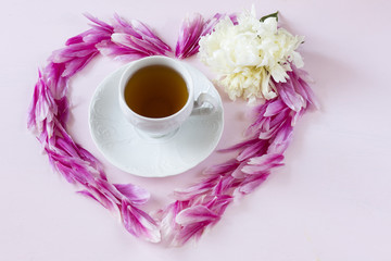 on a pink background a heart made of peony petals, a white peony and a cup of tea in the center of the composition