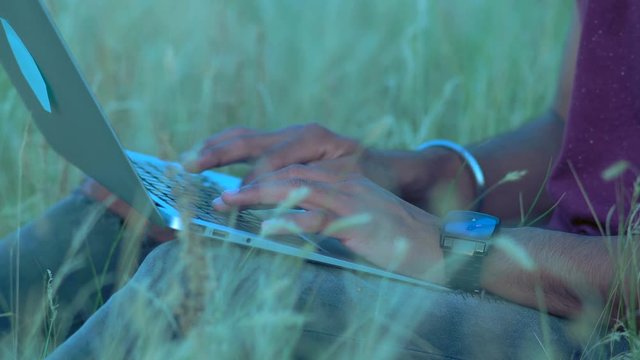 Close-up, Hands of an Indian Paren Sitting on the Grass Typing Text on the Laptop Keyboard