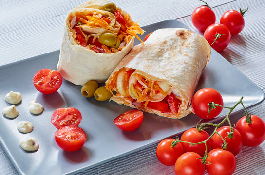 Eastern sandwich or healthy lavash snack with fresh vegetables and sauce on the gray plate decotated with cherry tomatoes, basil leaves. Traditional Iranian or Indian food. Arabic cuisine. Side view
