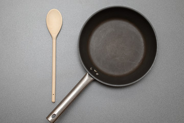 Silberne Teflonpfanne neben einem Kochlöffel aus Holz auf einem grauen Tisch