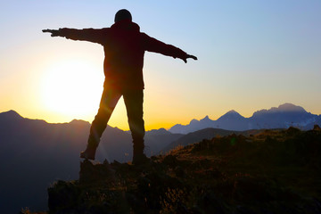 tourist with arms raised standing on the mountain at dawn.