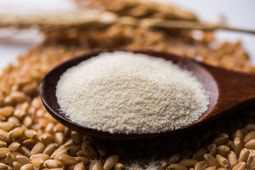 Raw unprepared semolina flour also known as Rava powder in Hindi in bowl or spoon. close-up isolated on white or moody background. selective focus