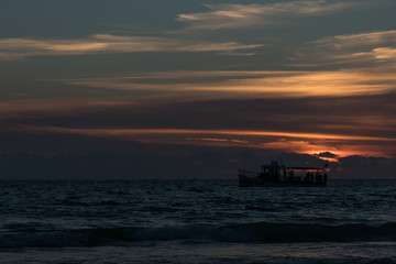 Fototapeta na wymiar Silhouette of boat on the horizon at sunset on the beach