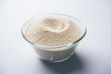 Raw unprepared semolina flour also known as Rava powder in Hindi in bowl or spoon. close-up isolated on white or moody background. selective focus