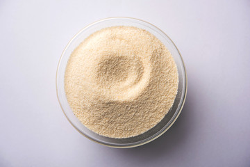 Raw unprepared semolina flour also known as Rava powder in Hindi in bowl or spoon. close-up...