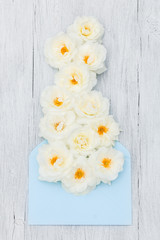 White rose flowers with yellow centers fall out of the blue envelope. Everything on a white, wooden background.