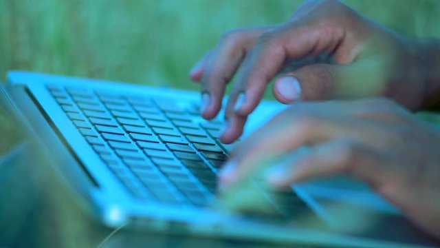 Close-up, Hands of an Indian Paren Sitting on the Grass Typing Text on the Laptop Keyboard
