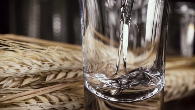 Spikelets of wheat behind a glass in which to pour ice vodka slow motion