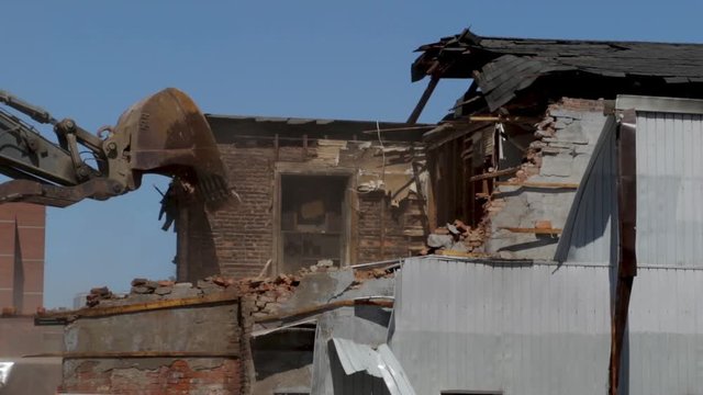 Construction demolition of an old abandon derelict home. Large crane with claw tearing down a brick wall of a home. Renovation and gentrification of old run down buildings. 