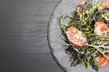 Authentic salad with arugula, tomatoes, sesame and olive oil on a black plate. Selected focus soft