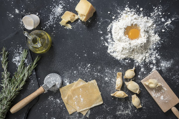 Italian cuisine ingredients over black surface. Heap of flour, olive oil and ravioli preparation to put a logo or sign