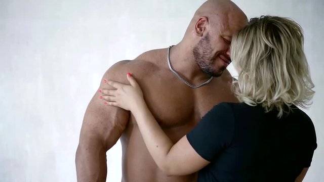 sporty brutal bald man and his woman with blonde hair hugging the white wall